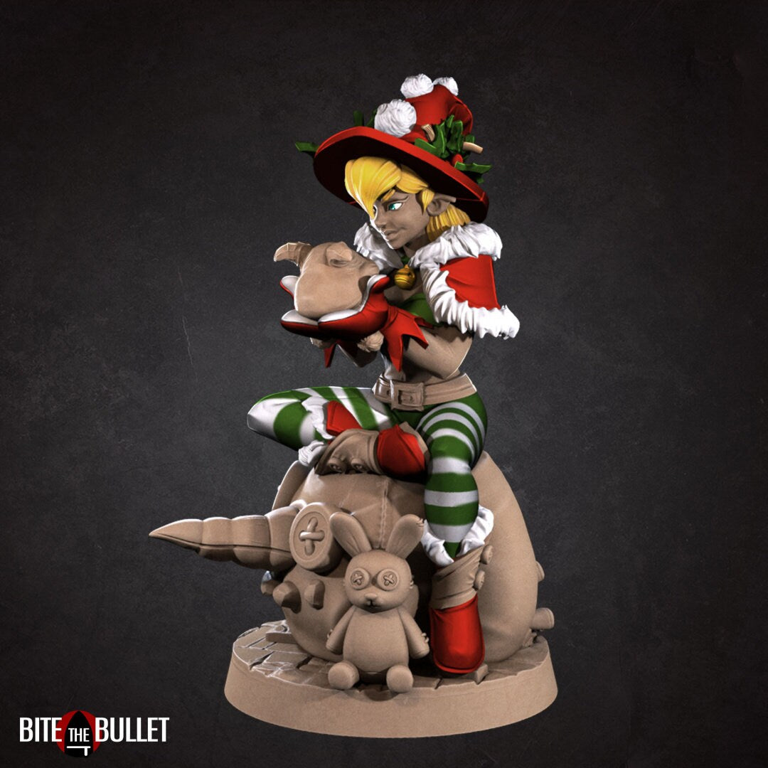 Christmas elf girl sitting on a toy snowman head, holding a toy that's sticking its tongue out at her. Resin miniature by Bite the Bullet.