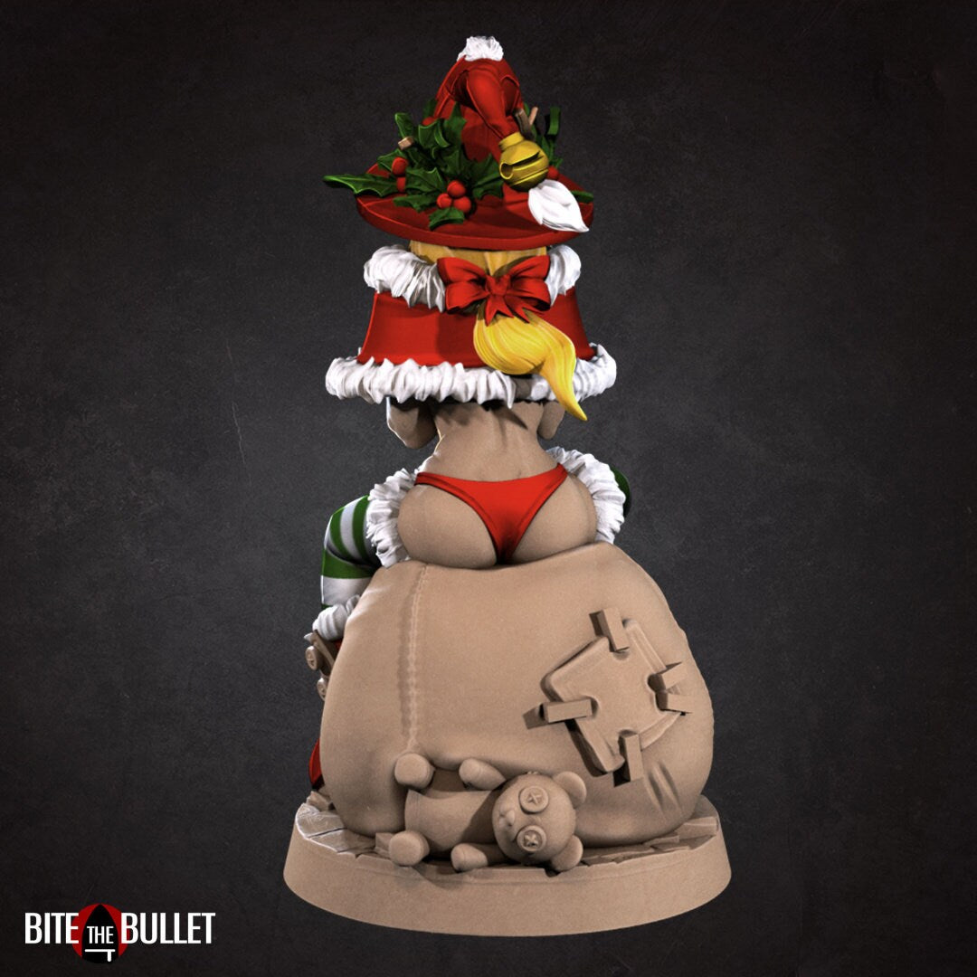 Christmas elf girl with a bare midriff and bikini bottom sitting on a toy snowman head, holding a toy that's sticking its tongue out at her. Resin miniature by Bite the Bullet.