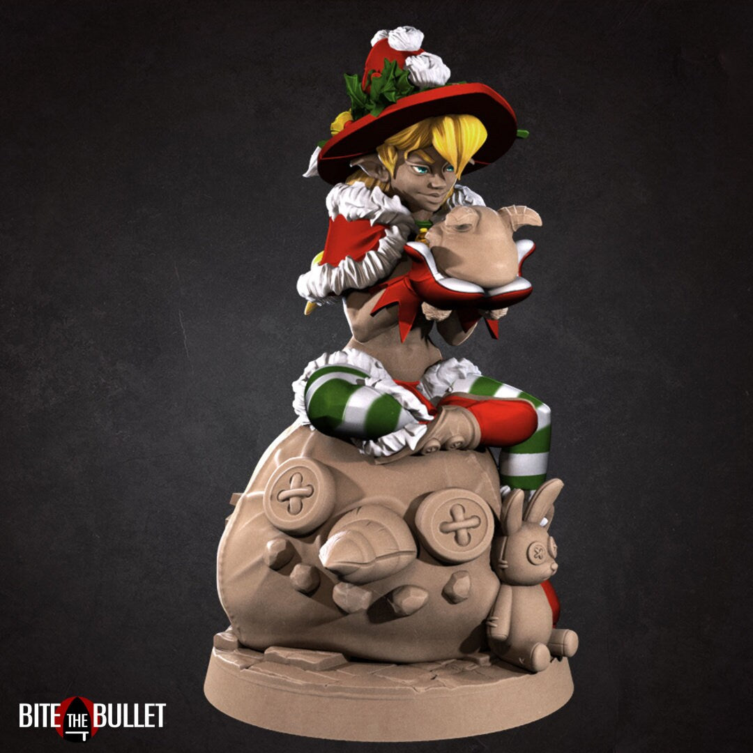 Christmas elf girl with a bare midriff sitting on a toy snowman head, holding a toy that's sticking its tongue out at her. Resin miniature by Bite the Bullet.