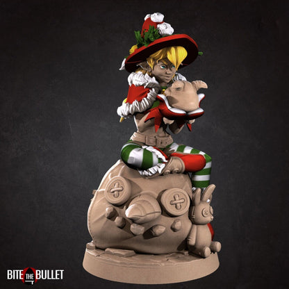Christmas elf girl sitting on a toy snowman head, holding a toy that's sticking its tongue out at her. Resin miniature by Bite the Bullet.